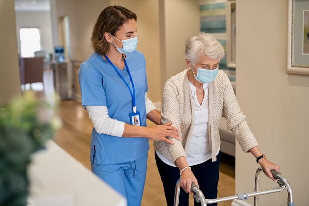 elderly woman being pushed by nurse with mask on.