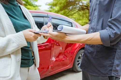 Person signing document beside damaged car door after traffic collision