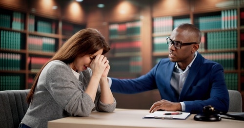 Woman covering face while meeting attorney at desk with legal books behind